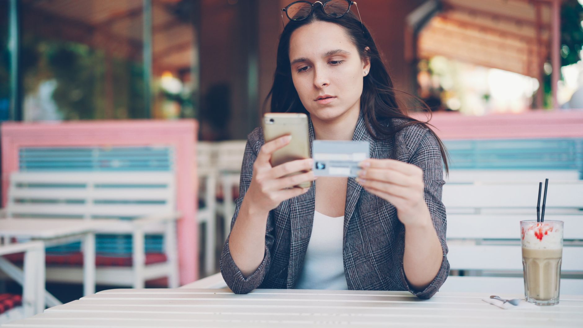 Mulher consultando o celular ao lado de uma xícara de café